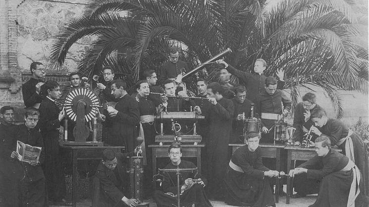 A historical black and white photo depicting a group of priests with various scientific instruments and equipment.