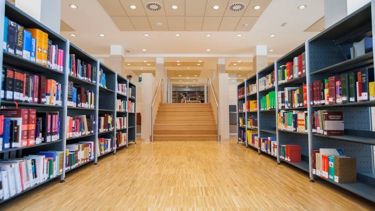 A spacious library with rows of colorful books on shelves and a staircase leading to another level.