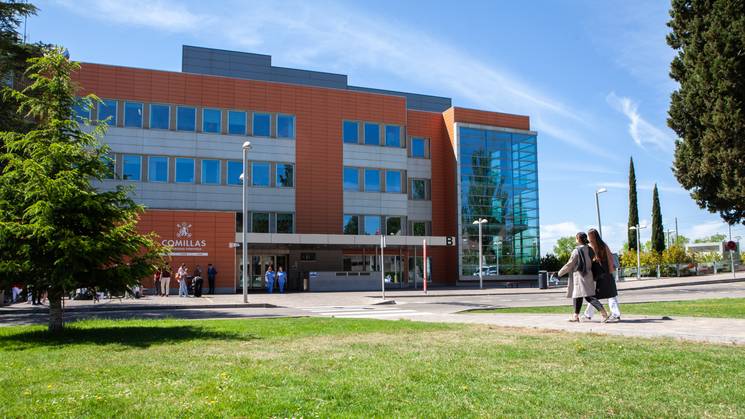 Edificio moderno situado en un campus con personas caminando por el área verde.