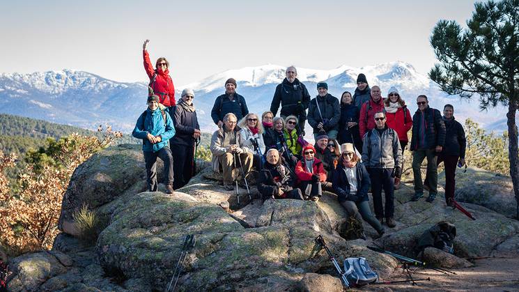 Un grupo de personas posando en una roca con montañas nevadas al fondo.