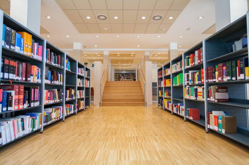 Una biblioteca moderna con estanterías llenas de libros y un área de escaleras al fondo.
