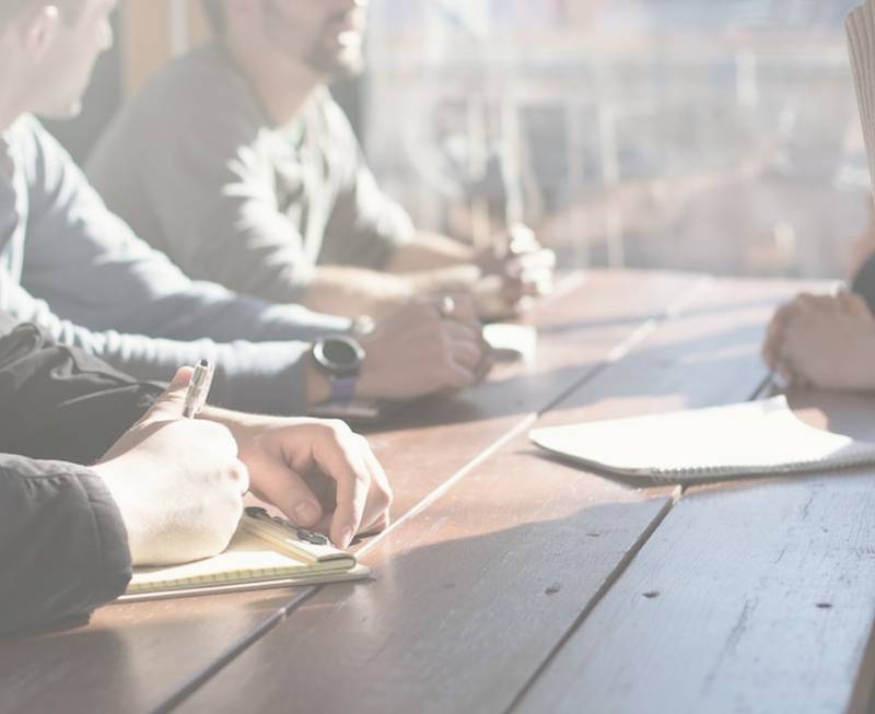 Un grupo de personas colaborando y escribiendo en una mesa de trabajo.