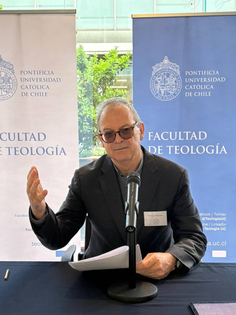 Una persona sentada frente a un micrófono en un evento de la Facultad de Teología de la Pontificia Universidad Católica de Chile.
