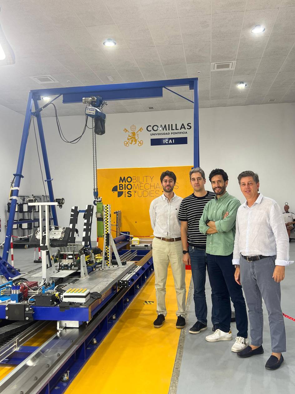 Four men standing in a laboratory with advanced mechanical equipment and a banner that reads 'Comillas ICAI'.