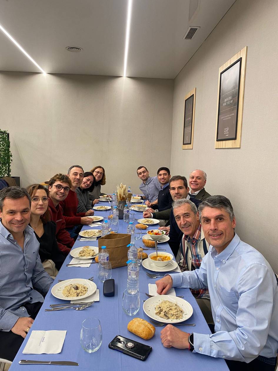 Un grupo de personas sonrientes disfrutando de una comida en una larga mesa.