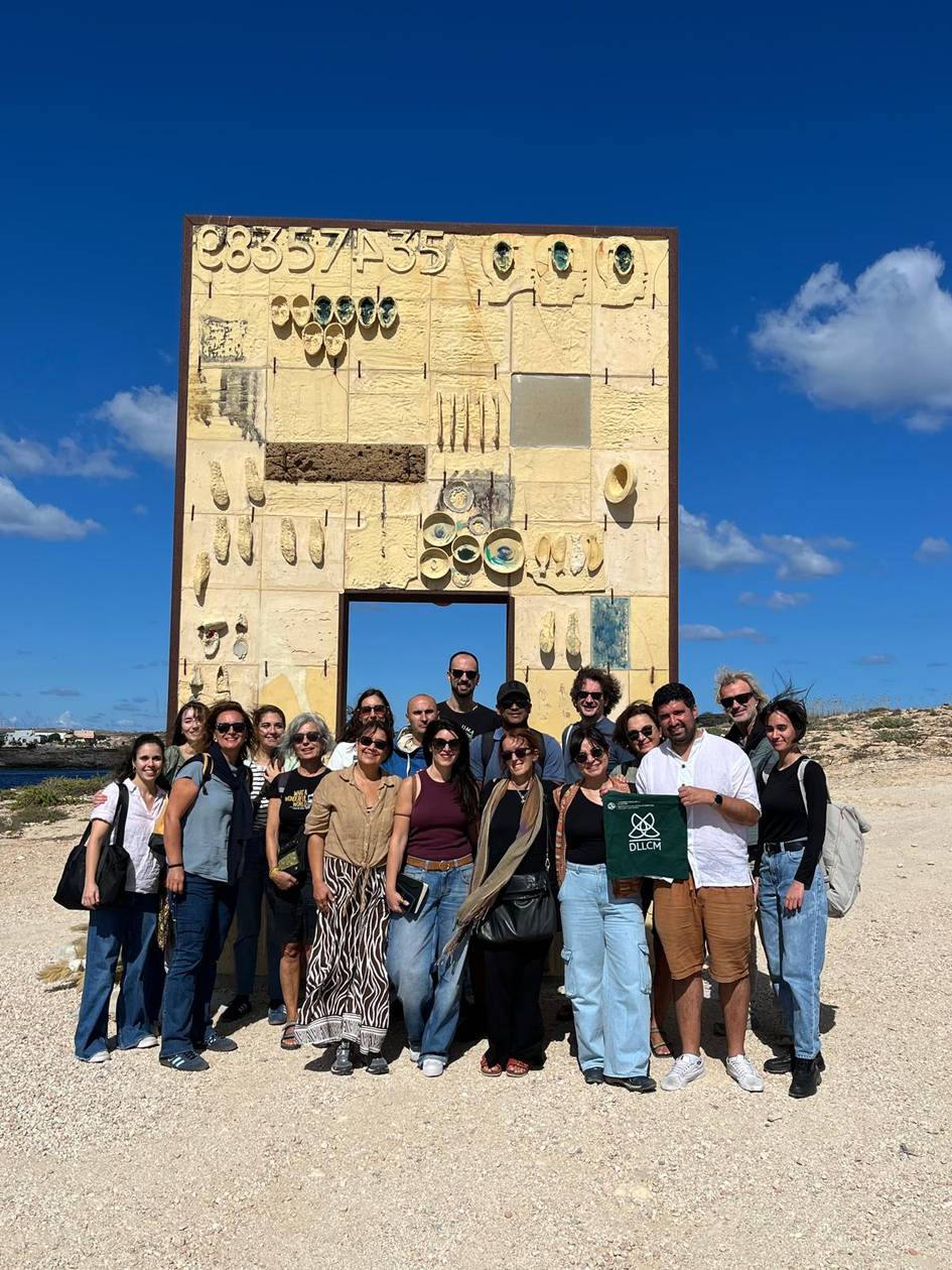 Una grupo de personas posando frente a una estructura artística en un paisaje abierto bajo un cielo azul.