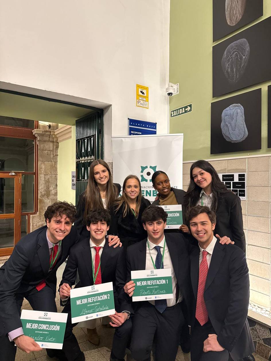 Un grupo de estudiantes sonrientes posando con carteles de reconocimiento en un evento académico.