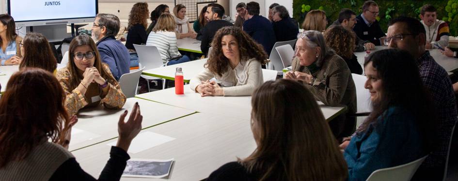 A group of people are sitting around a table in a lively discussion in a conference or workshop setting.