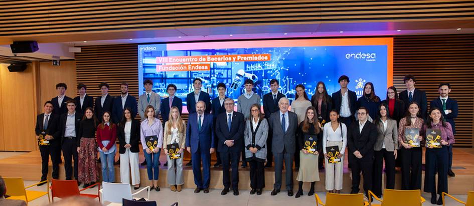 Un grupo de personas posando en un evento, con un fondo de pantalla que muestra logotipos y texto referente a un encuentro de bachilleres premiados.