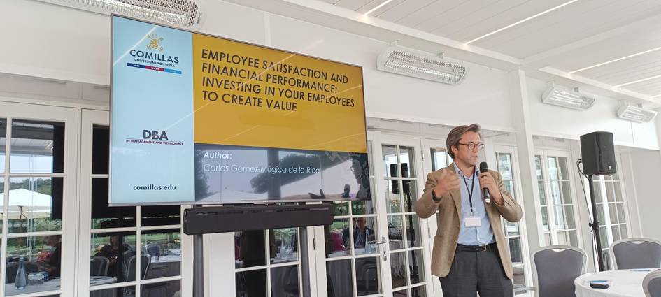 A man presents a lecture on employee satisfaction and finance performance in front of a digital screen inside a modern room.