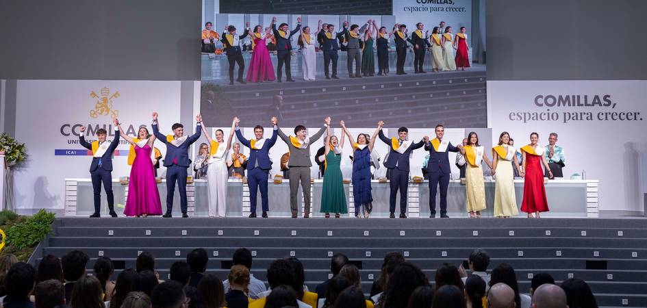 Un grupo de graduados celebra en un escenario alzando los brazos ante una audiencia.