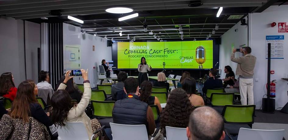 Personas atendiendo a una presentación en un evento llamado 'Comillas Cast Fest', en un ambiente informal y moderno.