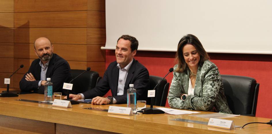 Three people sitting at a conference table, speaking and smiling in a panel discussion.