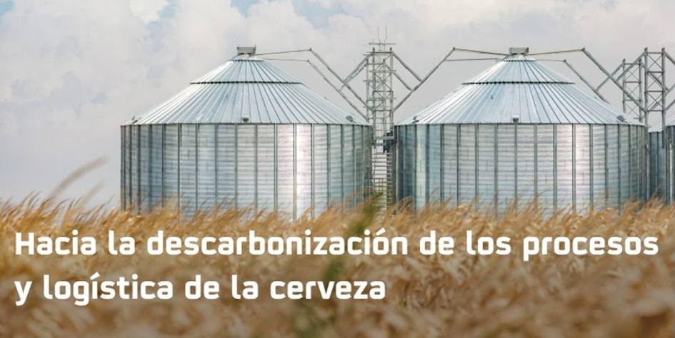 La imagen muestra silos metálicos en un campo de trigo bajo un cielo nublado, acompañados de un mensaje sobre la descarbonización en la logística de la cerveza.