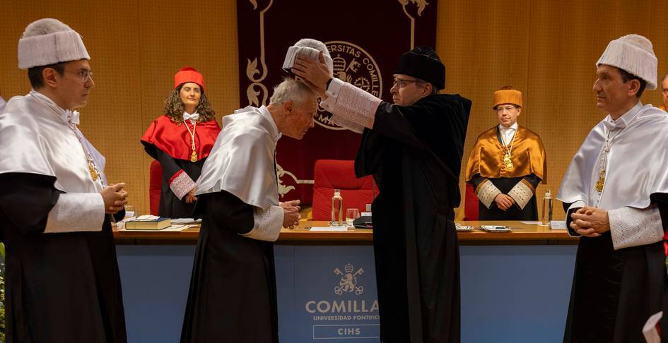 La ceremonia de un homenaje académico con la entrega de un birrete a un distinguido profesor en un evento solemne.