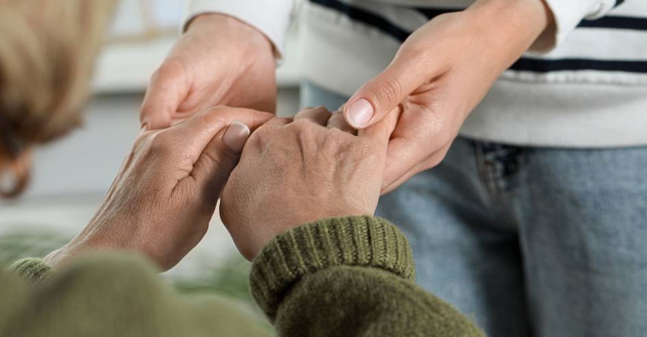 Una persona joven está sujetando la mano de una persona mayor en un gesto de apoyo y cuidado.