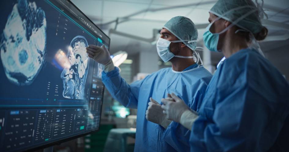 Dos médicos examinan imágenes médicas en una pantalla en un entorno quirúrgico.
