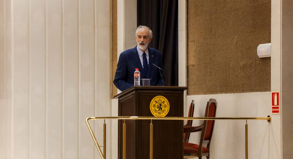 A man with a white beard speaking at a podium in a conference hall.