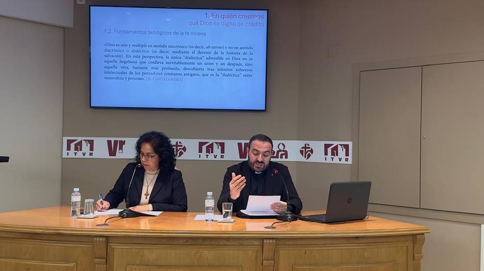 Un hombre y una mujer participan en una presentación frente a una pantalla con información en una sala de conferencias.
