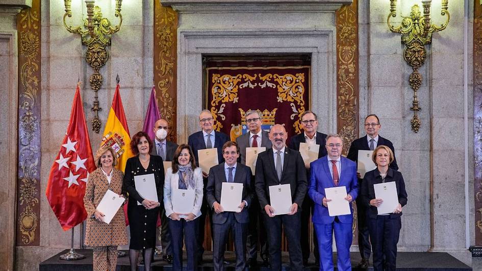 A group of people holding certificates inside an ornate hall with flags in the background.