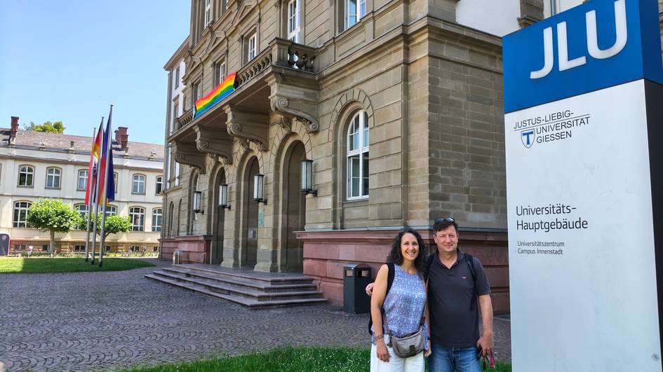 Una pareja sonriente posa frente al edificio principal de la Universidad Justus Liebig en Giessen, Alemania.