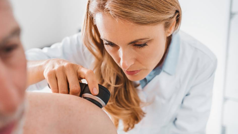 Una médica examina la piel de un paciente con un instrumento especializado.