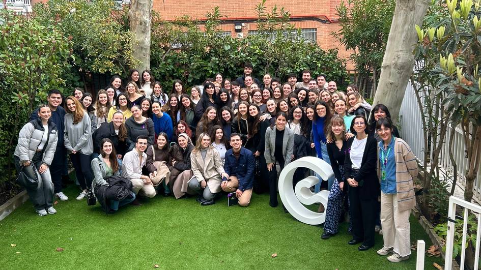 Un grupo grande de personas posando juntas en un jardín con un logo blanco en el centro.