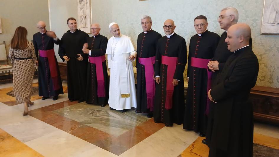 Un grupo de sacerdotes y un líder religioso posan juntos en una sala del Vaticano.