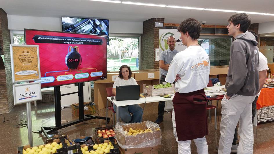 Un grupo de estudiantes observa atentamente una presentación interactiva sobre frutas en un evento educativo.