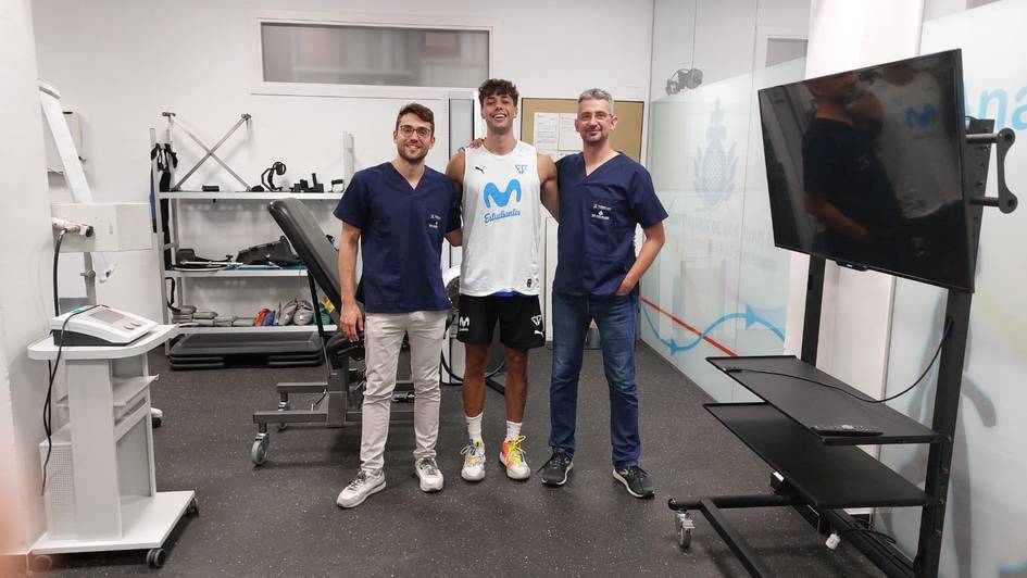 Three men standing in a sports rehabilitation center, surrounded by modern fitness equipment.