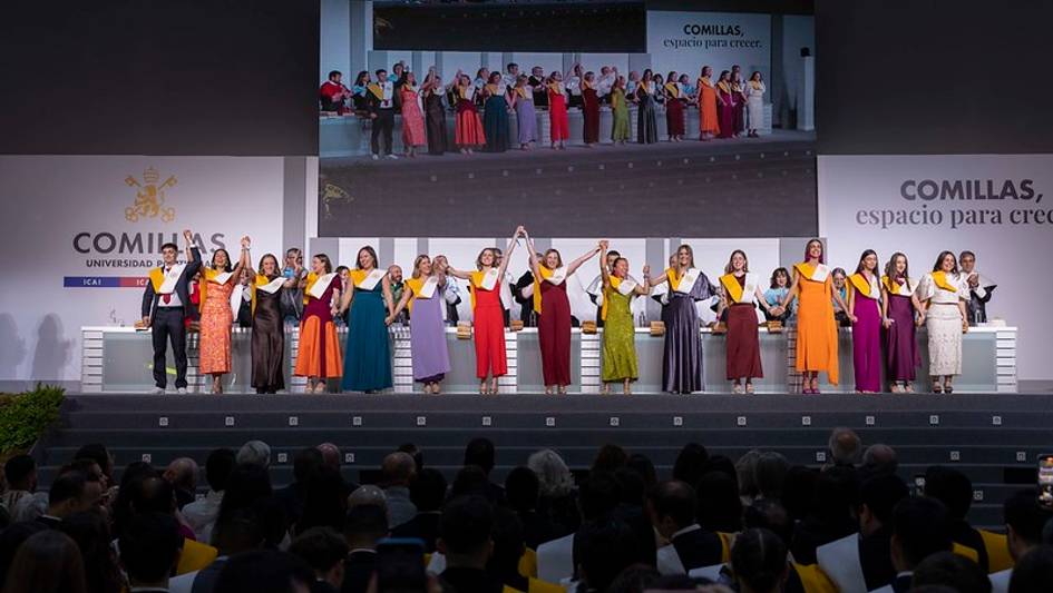 Ceremonia de graduación con un grupo de personas en trajes coloridos en el escenario de una universidad.