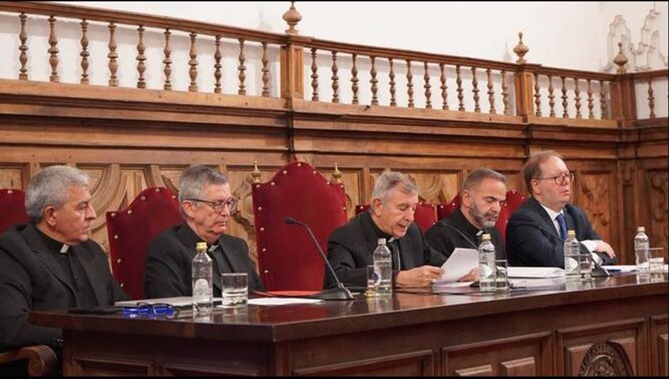 Cinco hombres sentados en una mesa larga durante una reunión en una sala elegante con sillas de respaldo alto.