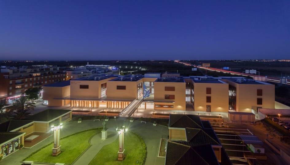 A panoramic view of a modern building at dusk with illuminated lights and a clear sky.