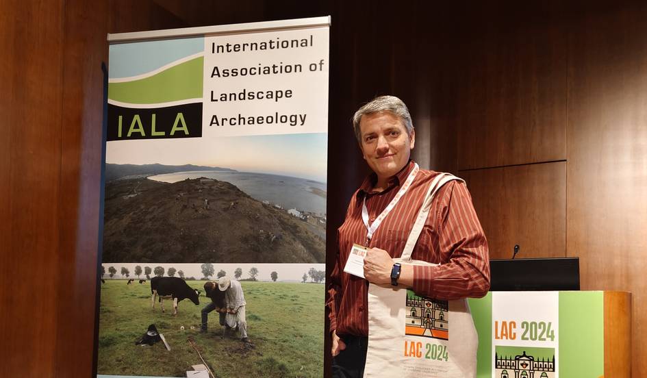 A person standing next to a banner for the International Association of Landscape Archaeology conference.