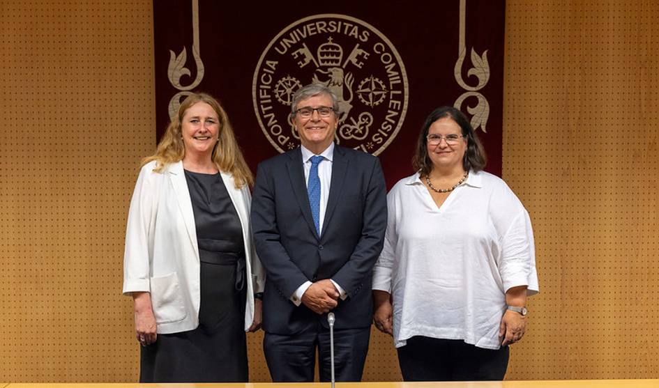 Tres personas posan juntas en un evento formal en una universidad.