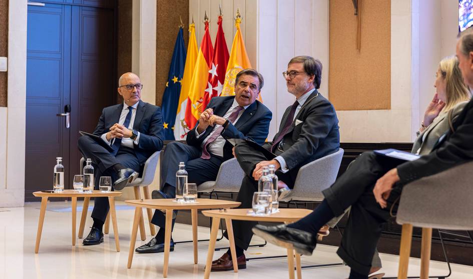 Un grupo de cuatro personas discute durante un evento en una sala con banderas de España.
