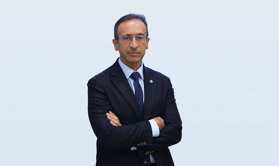 A man in a business suit standing with his arms crossed against a light background.