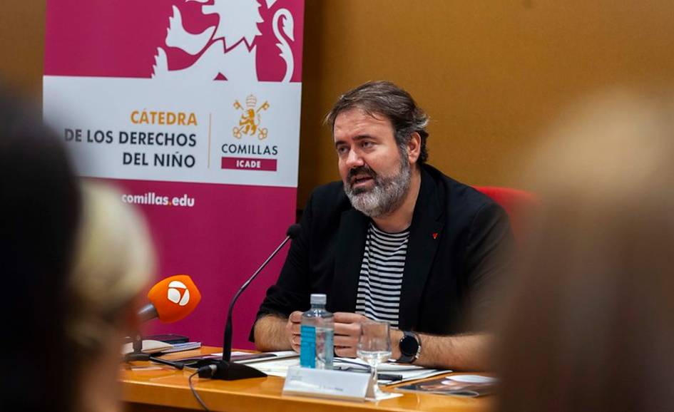 A man speaking at a seminar in a room with a banner titled 'Cátedra de los Derechos del Niño' in the background.