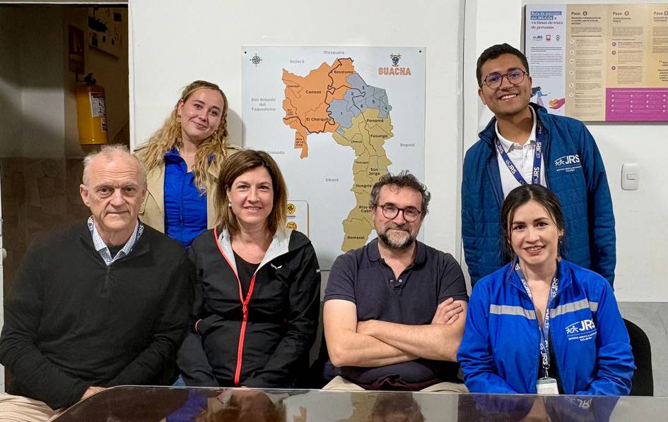 A group of six people smiling at a table with a map of La Guajira in the background.