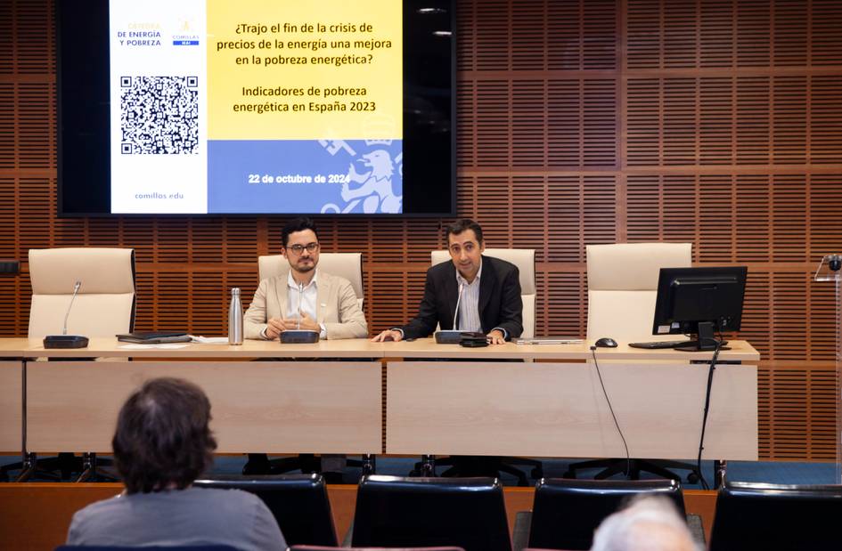 Two men presenting at a conference on energy poverty, with a screen displaying a QR code and text in Spanish.