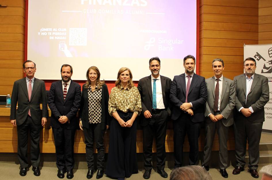 Un grupo de siete personas posando sonrientes frente a un escenario con logos de empresas y textos sobre finanzas.