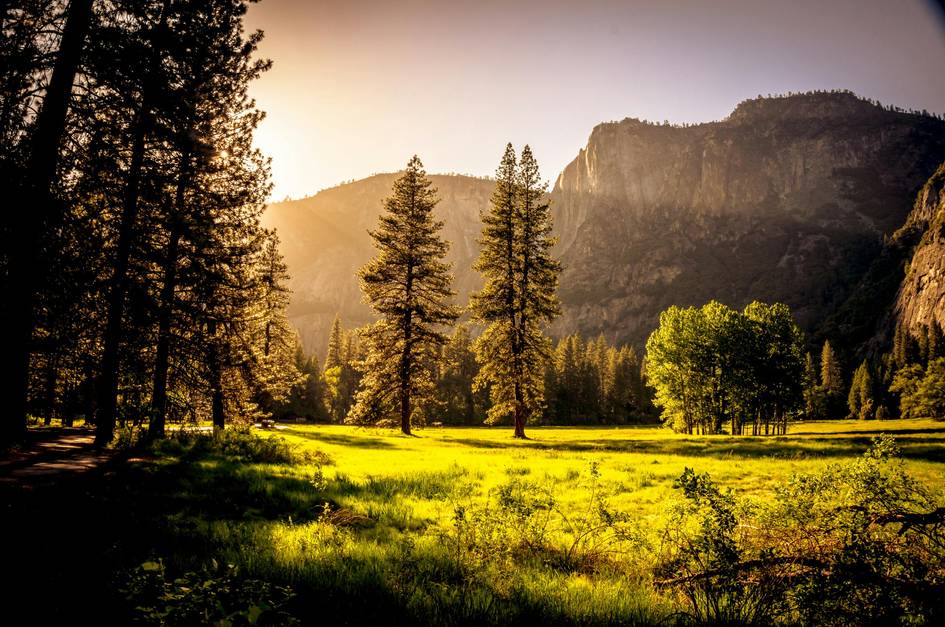 Paisaje de un valle con árboles y montañas al atardecer, bañado en luz dorada.