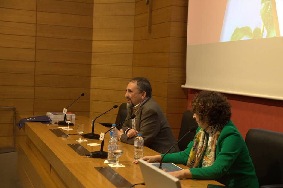 Una conferencia en un salón con dos ponentes hablando frente a un público.