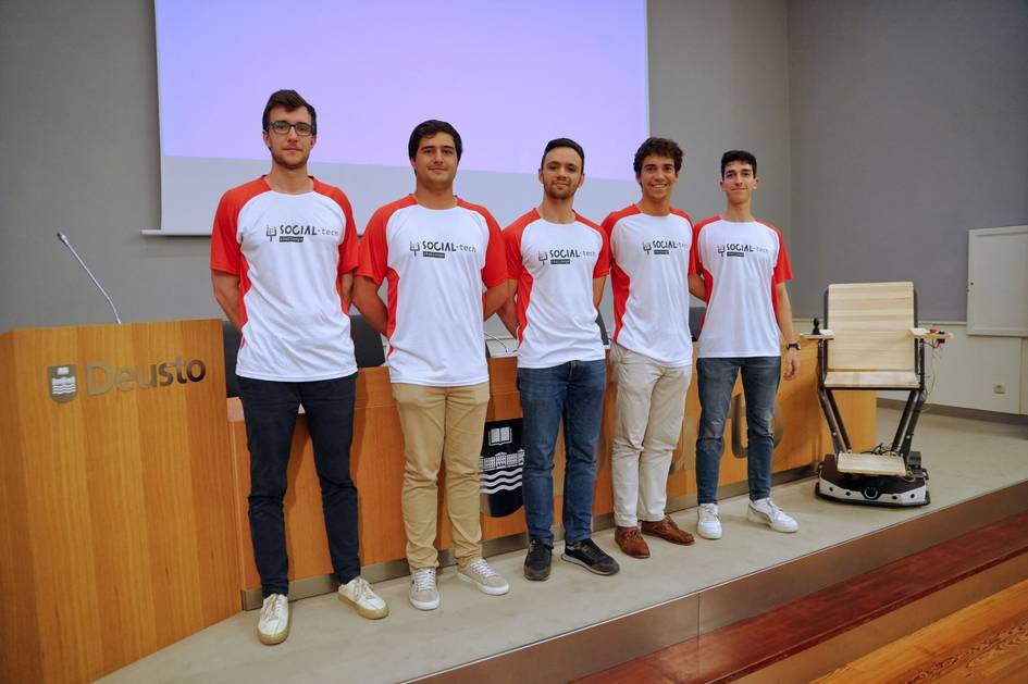 A group of five young men wearing red and white team t-shirts standing in a conference room.