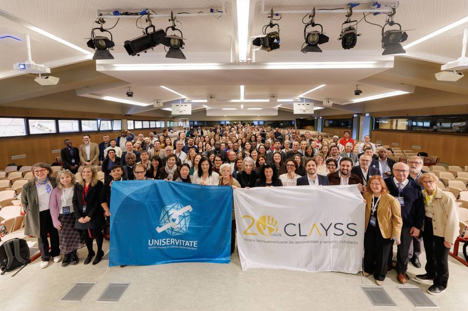 Grupo numeroso de personas posando en un evento, sosteniendo banderas de Universitate y CLAYSS.