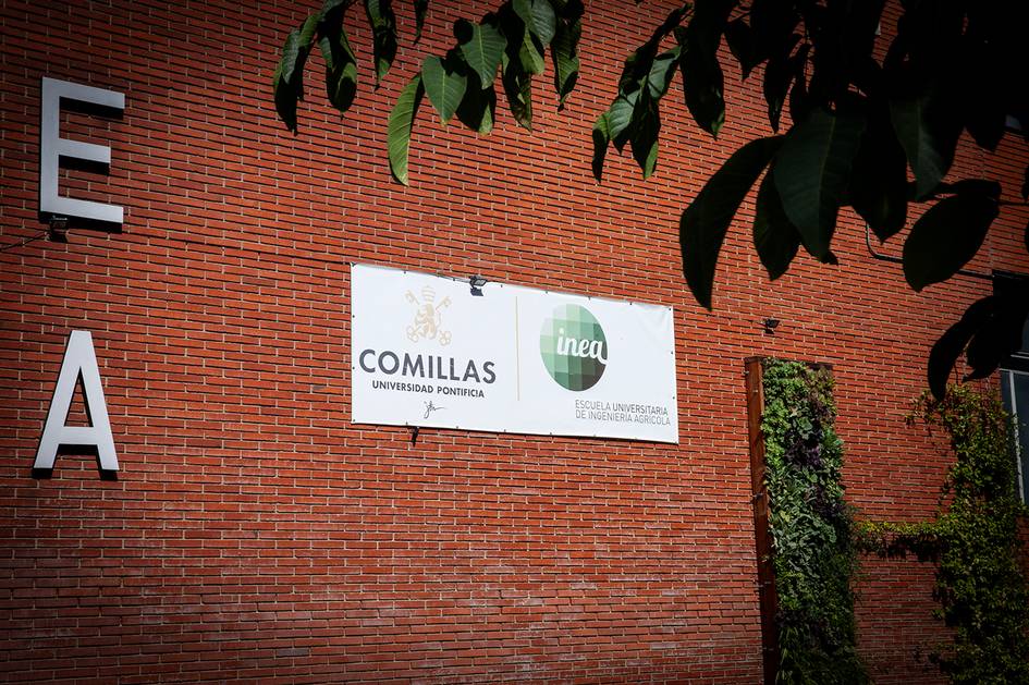 La imagen muestra un cartel de la Universidad Pontificia Comillas con el logotipo de INEA en una pared de ladrillo.