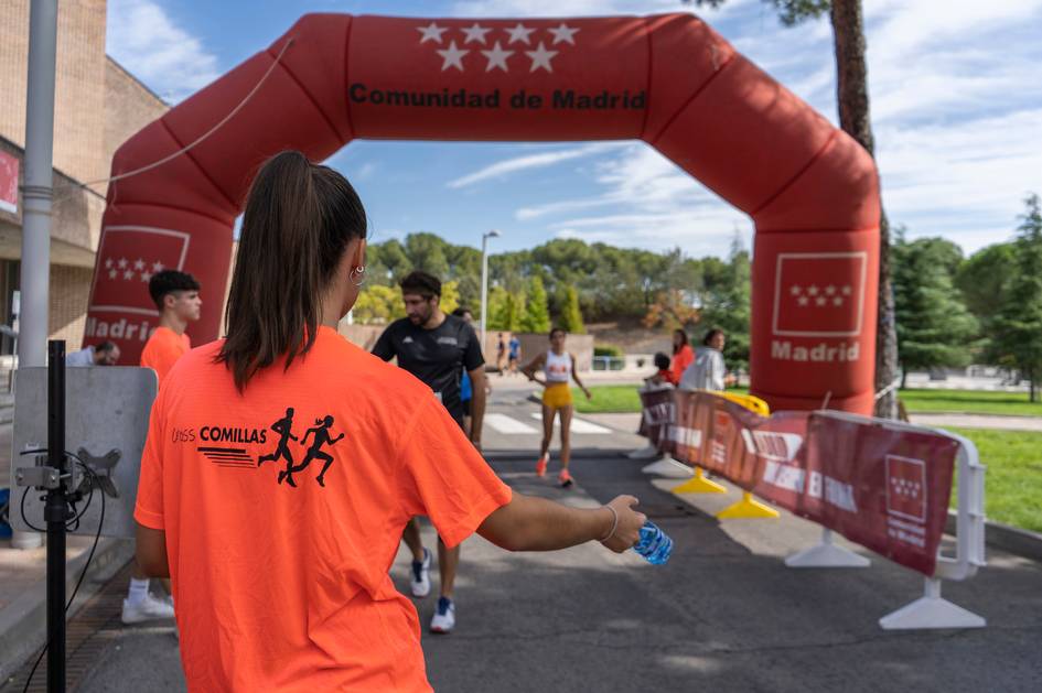 Una mujer con una camiseta naranja ayuda a los corredores en una carrera en Madrid.