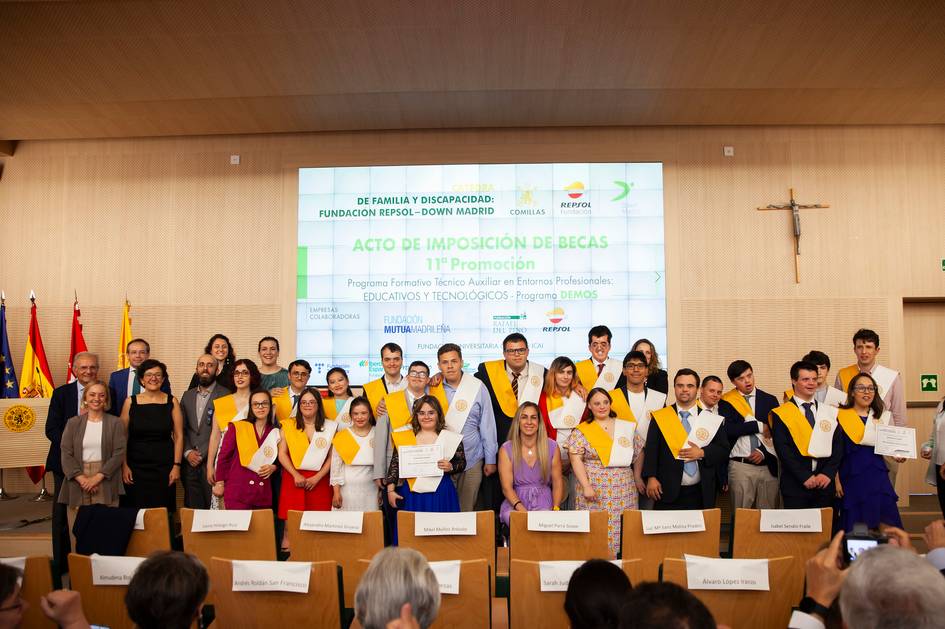 A group of students wearing sashes stands together at a scholarship award ceremony in a formal hall.