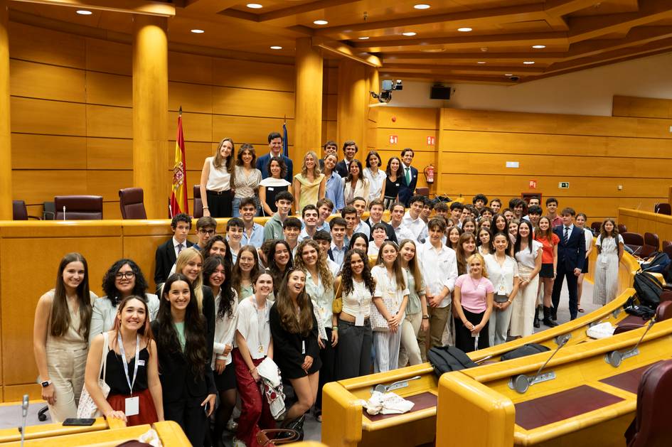 A large group of young students gathered inside a parliamentary or conference hall, smiling for a group photo.