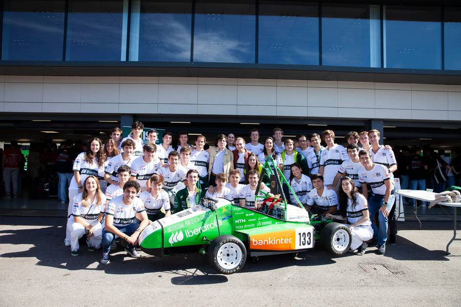 A group of young people posing with a green racing car in front of a modern building.